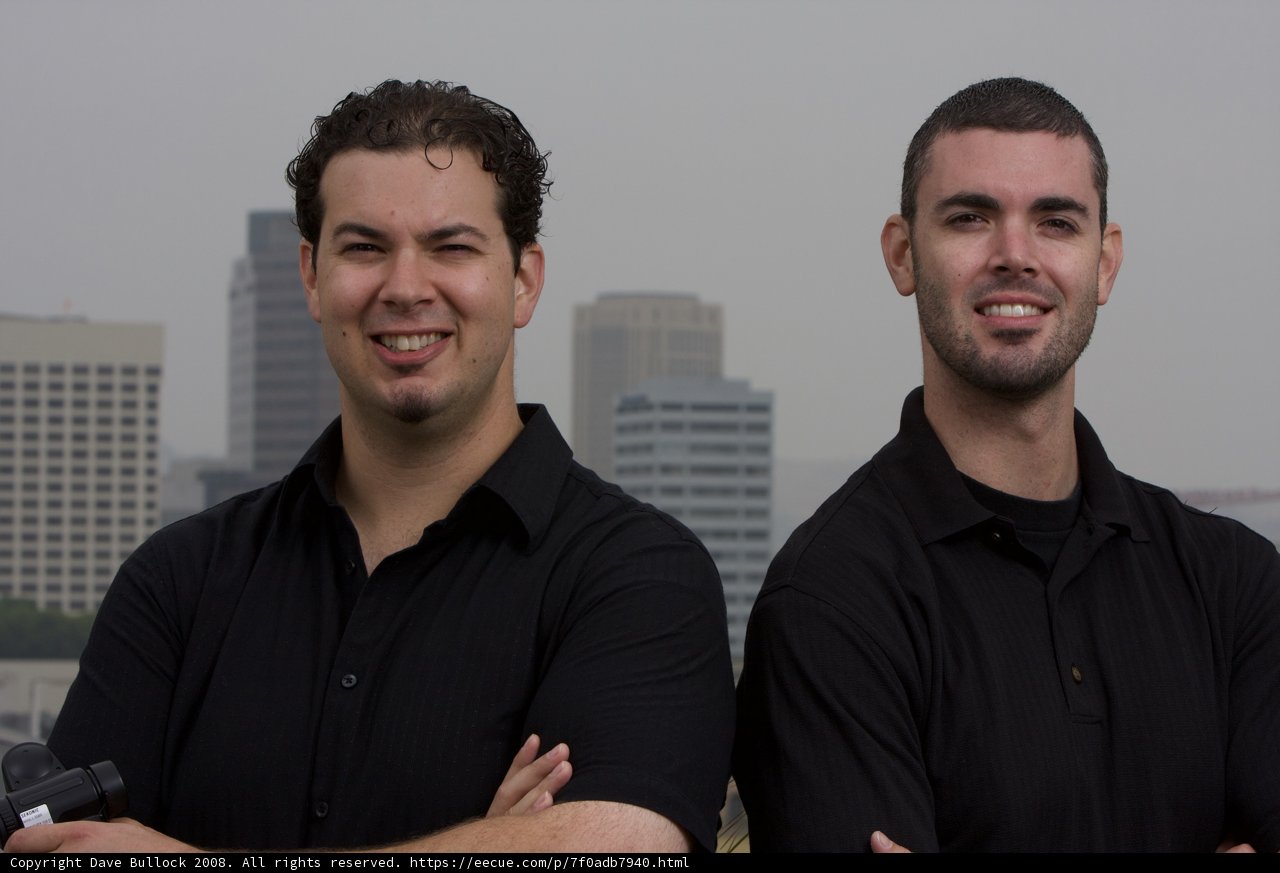 Two men in black shirts posing in front of a skyscraper