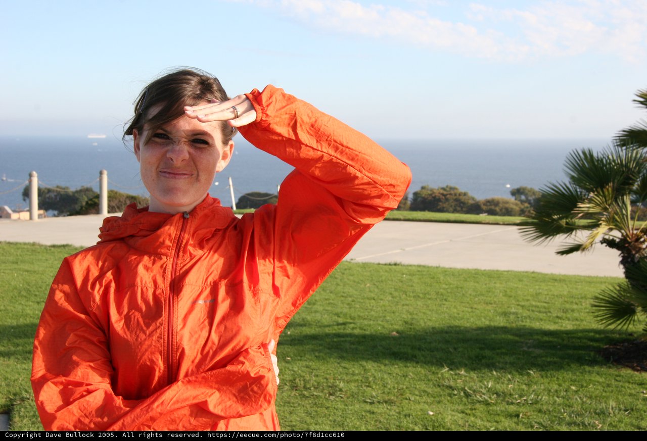 Woman in Orange Jacket Shielding Eyes by Coast