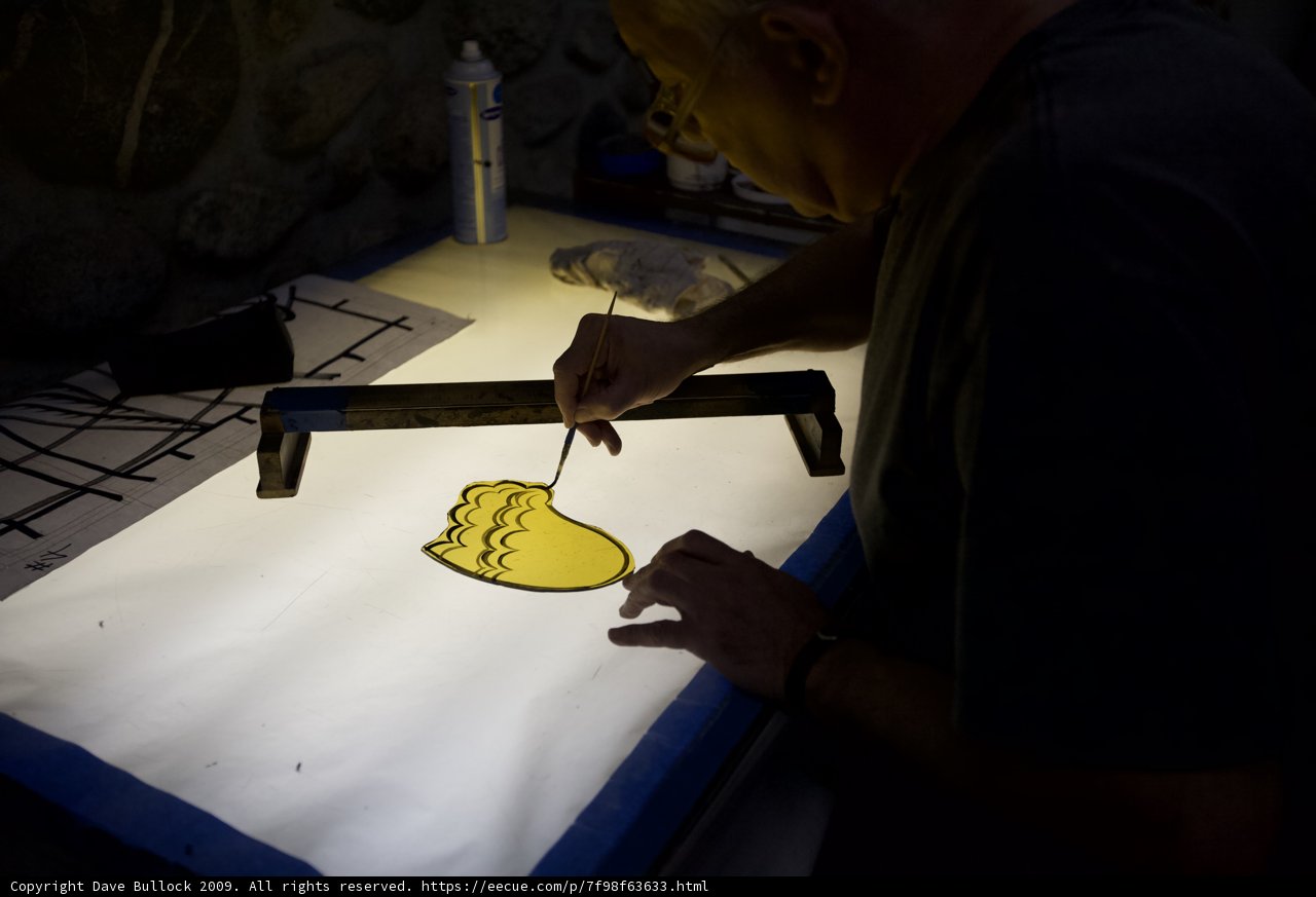 Working on Art: A Man Crafting with a Tool on a Yellow Surface