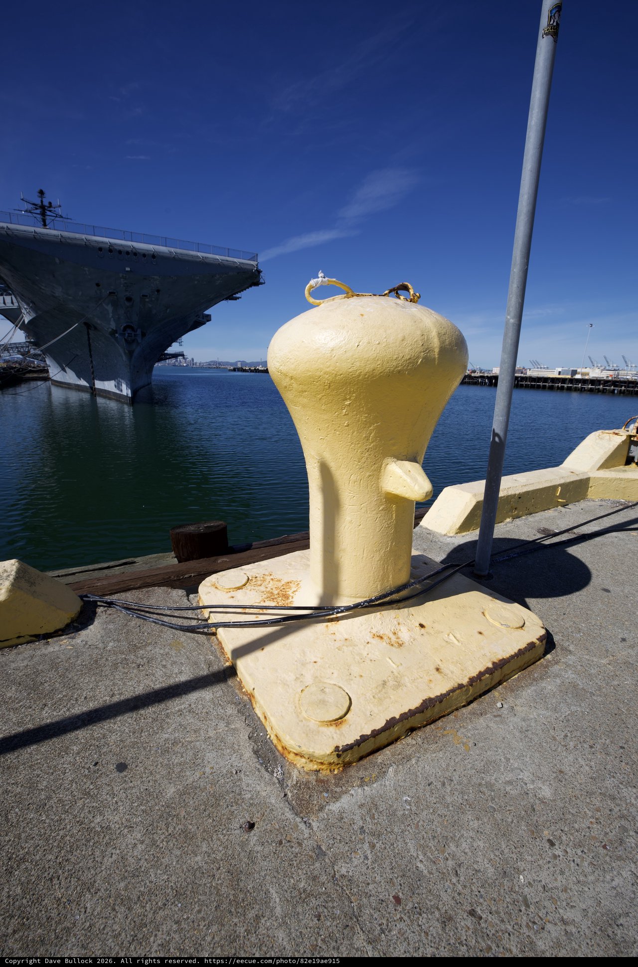 Yellow Mooring Bollard at Naval Harbor with Aircraft Carrier