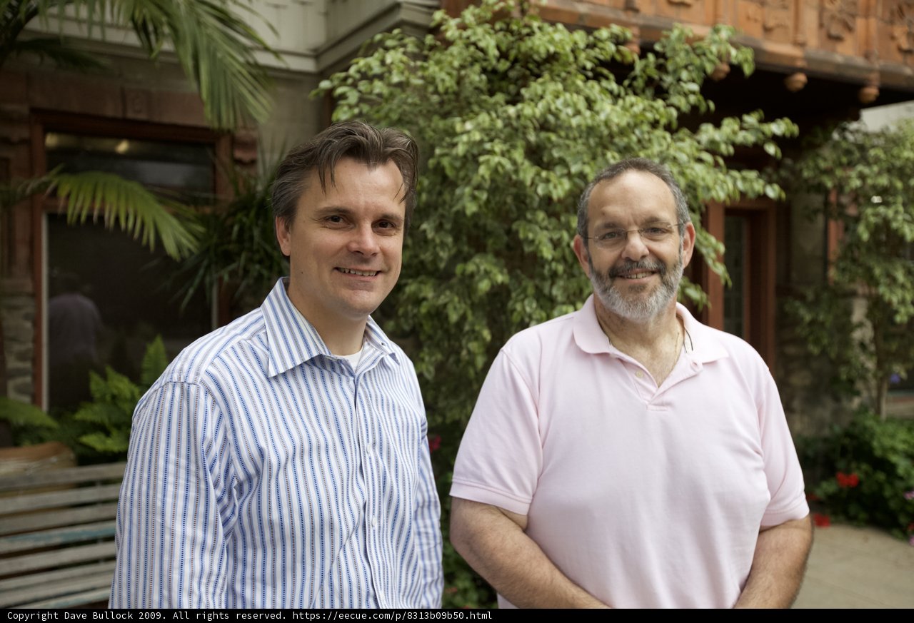Two Men Posed in Front of Foliage-Adorned Building