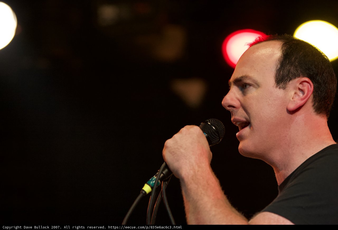 Rocking the Crowd Caption: A male singer performs at a concert, singing into a microphone while bathed in the spotlight and surrounded by an enthusiastic crowd.