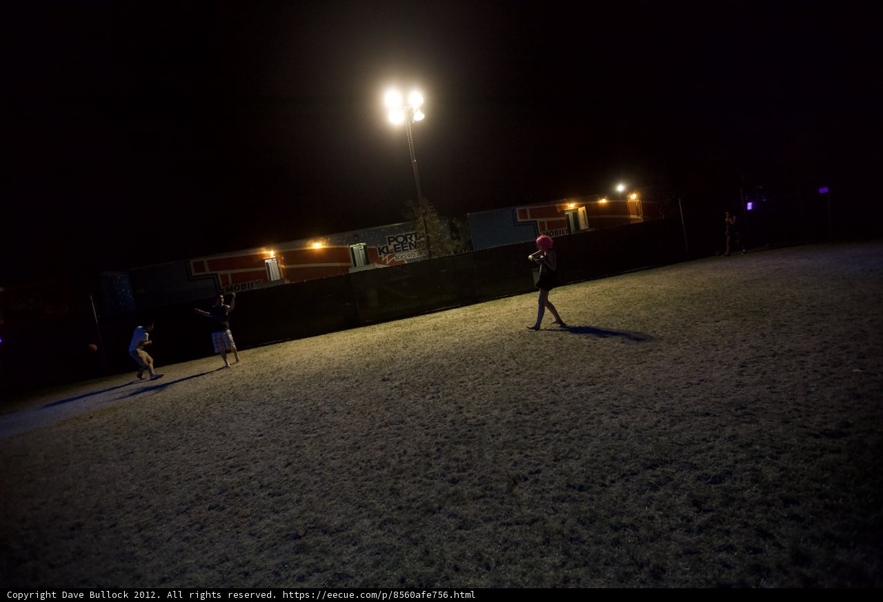 Nighttime Soccer Match Caption: A group of four people play soccer under the night sky, illuminated by the bright lights on a nearby lamp post.