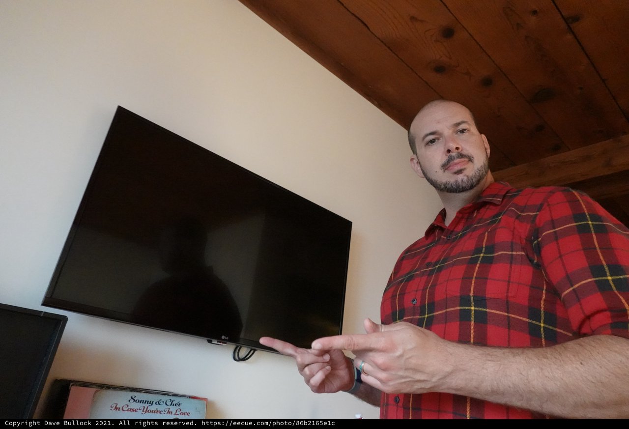 Man in Plaid Shirt Gesturing Toward TV