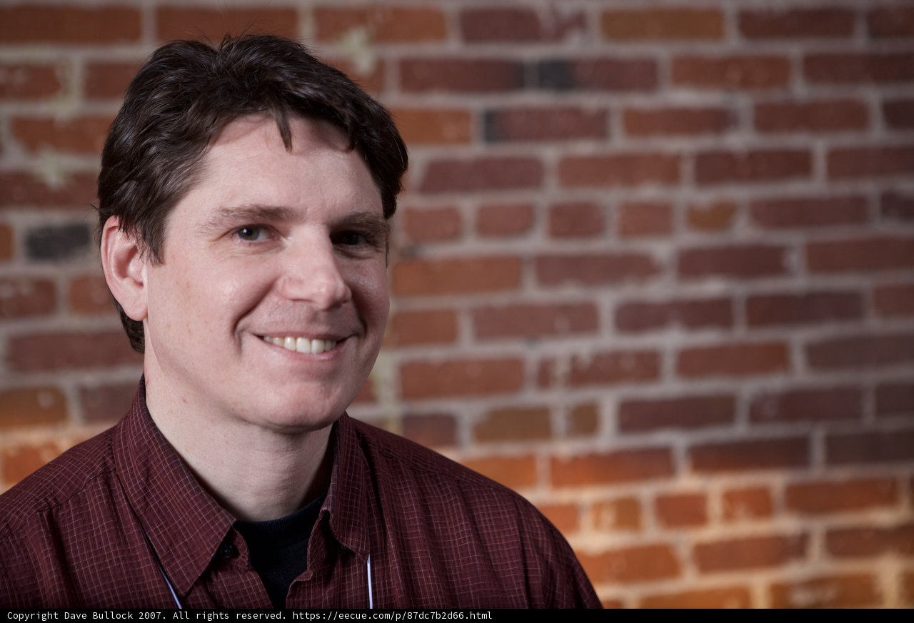 Red Shirted Man Poses in Front of a Brick Wall