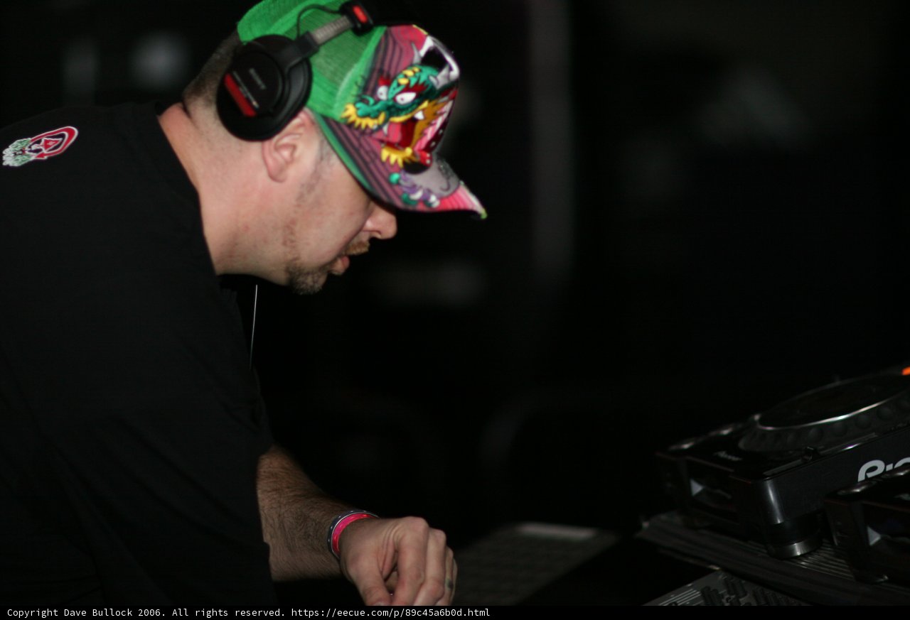 DJ in Action Caption: A male entertainer wearing a baseball cap, headphones, and a fingerless glove, while working with his turntable during a musical performance in 2006.
