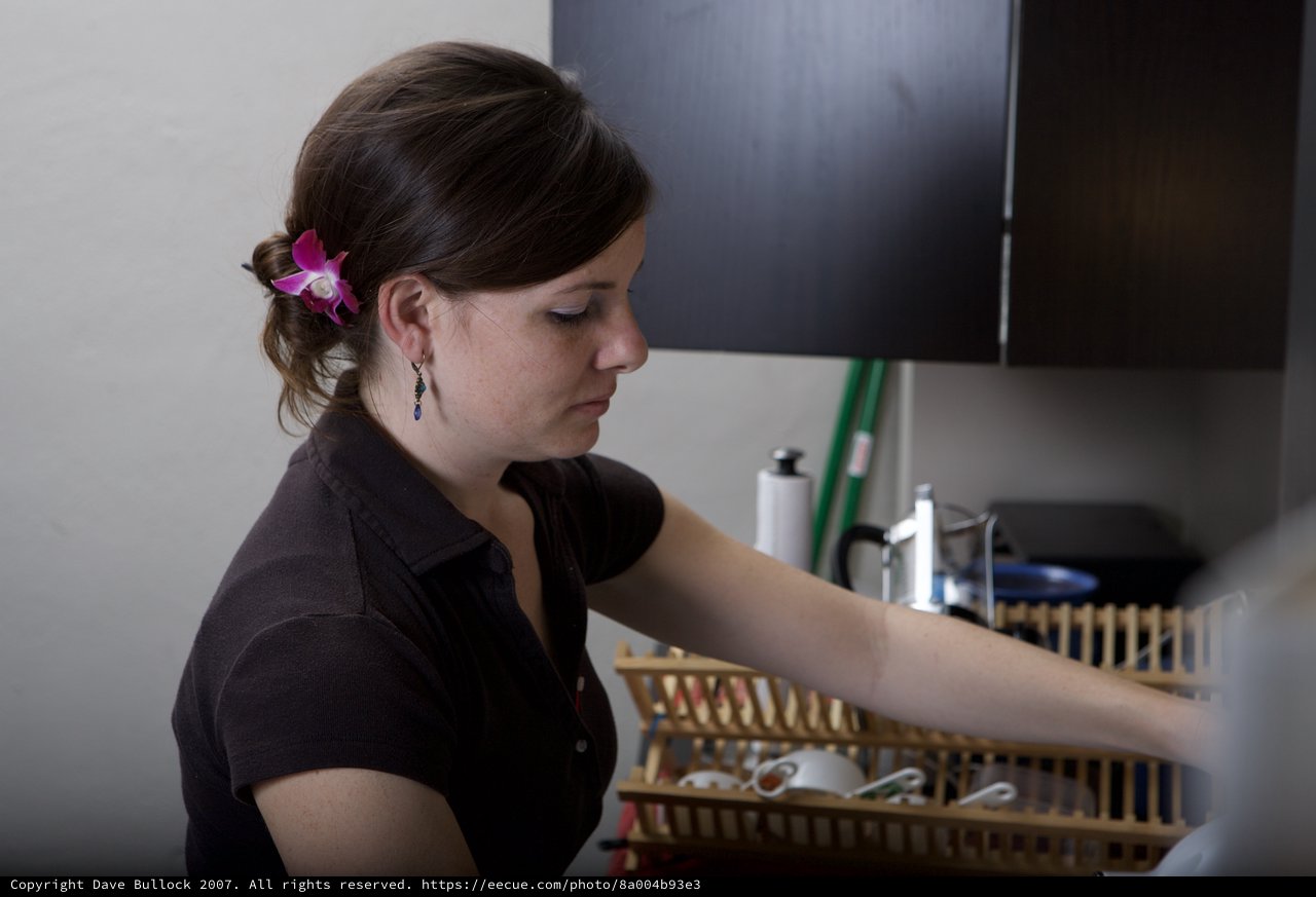Woman with Orchid Arranges Dishes in Kitchen