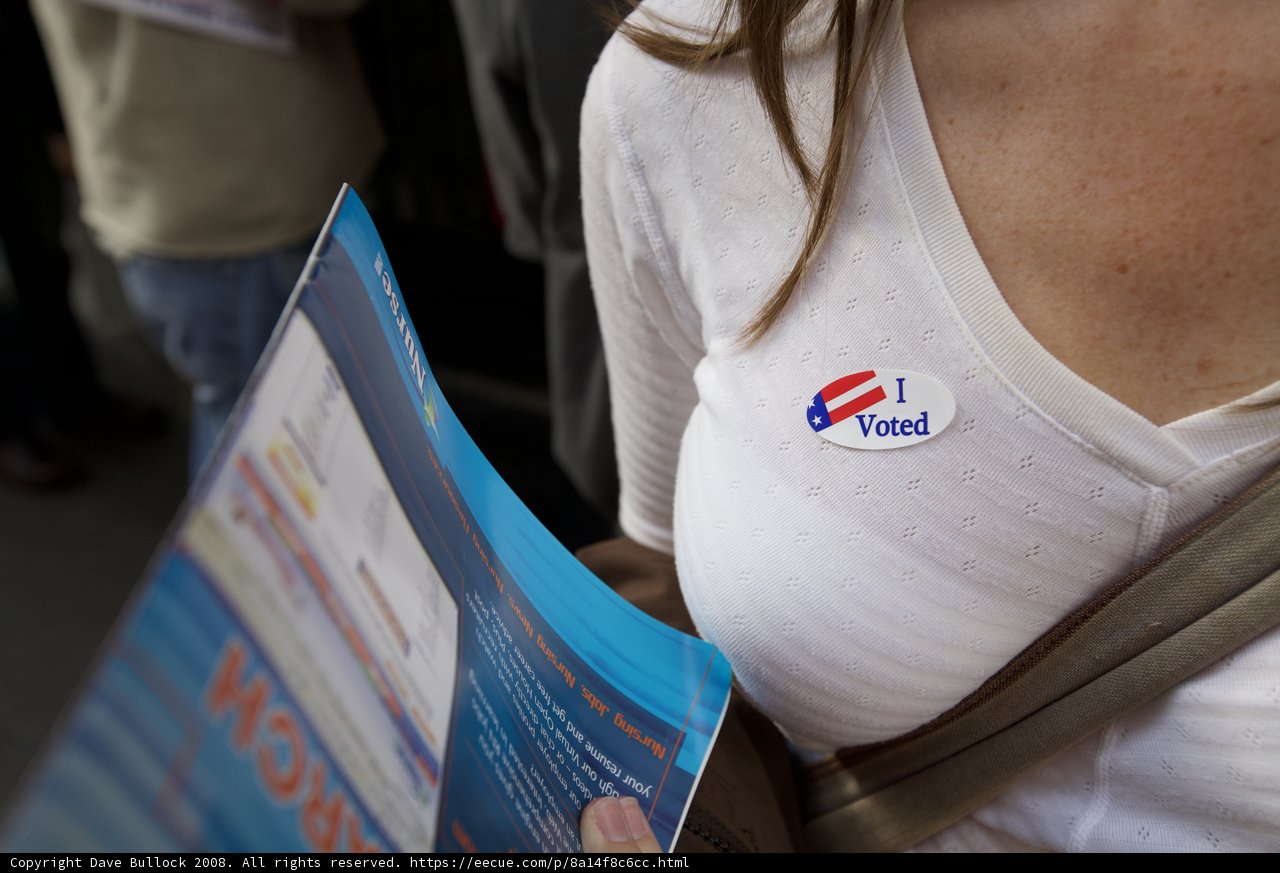 Showing Political Support Caption: A woman proudly holds a sign featuring a political party logo on election day while surrounded by three other individuals wearing campaign t-shirts.