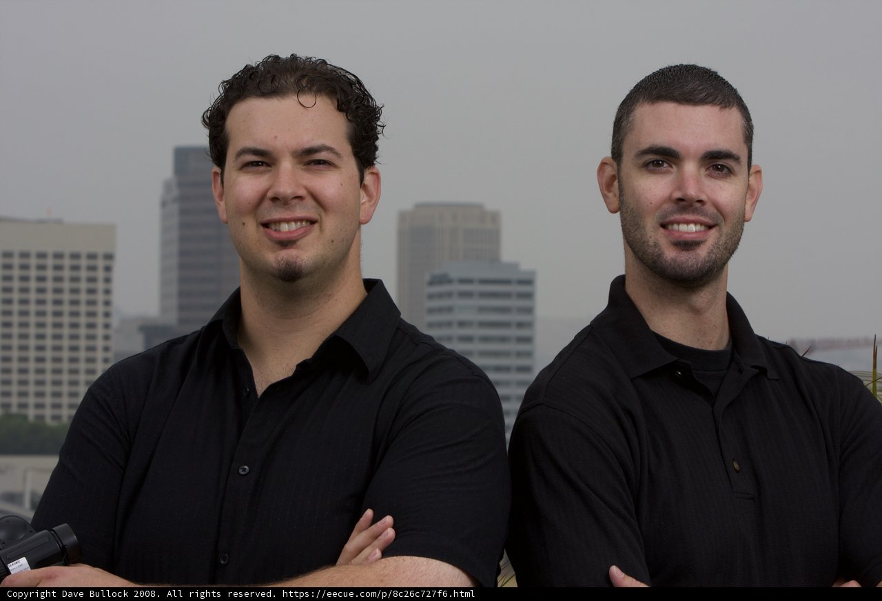 Two Happy Men in Black Shirts Pose in Front of Skyscraper