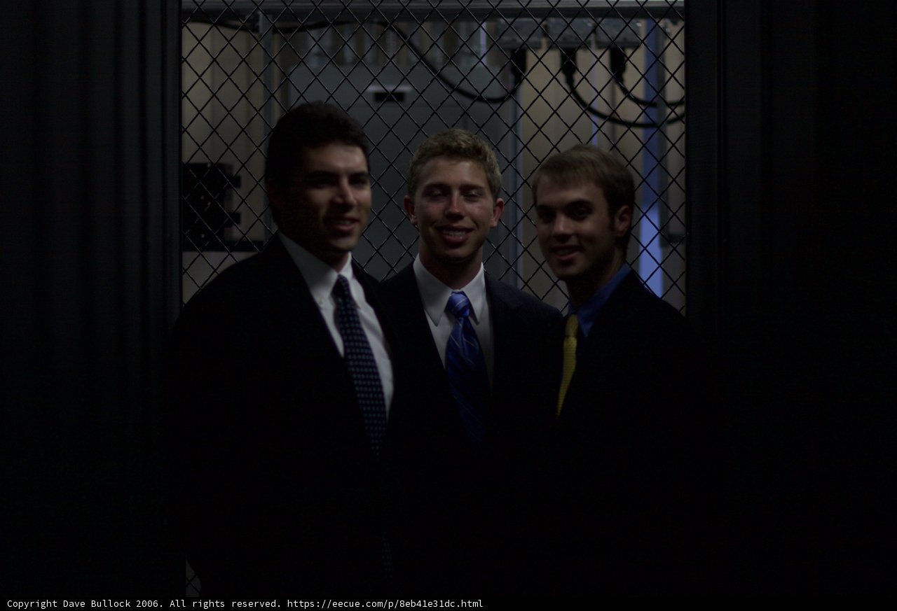 Three Men in Suits Pose in Front of Fence