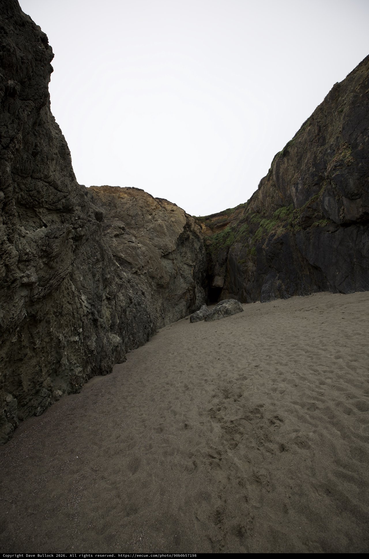 Dark Cave Opening Between Towering Coastal Sea Cliffs
