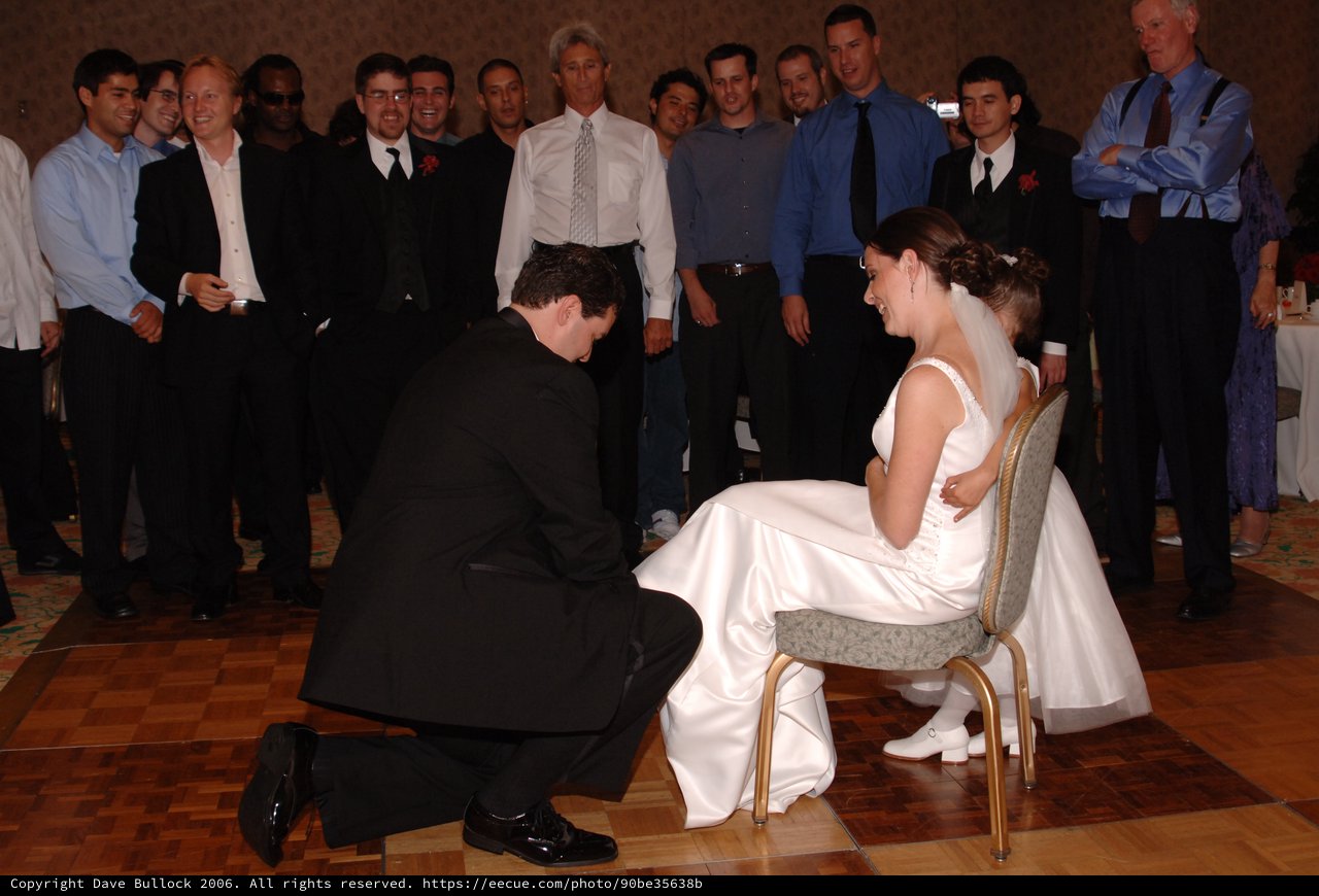 Groom Retrieves Garter from Laughing Bride at Reception