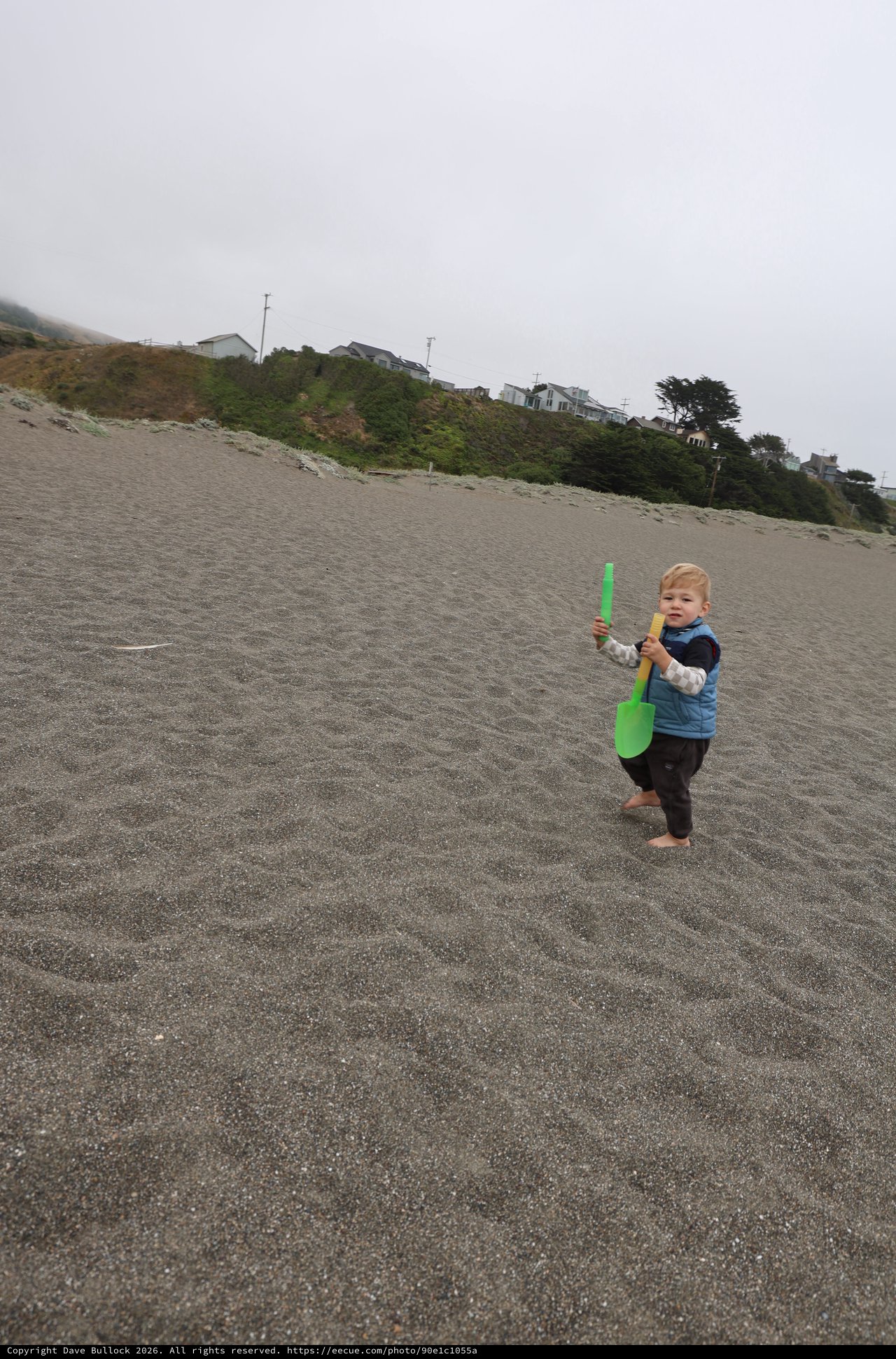 Toddler Explores Foggy Beach with Green Shovel