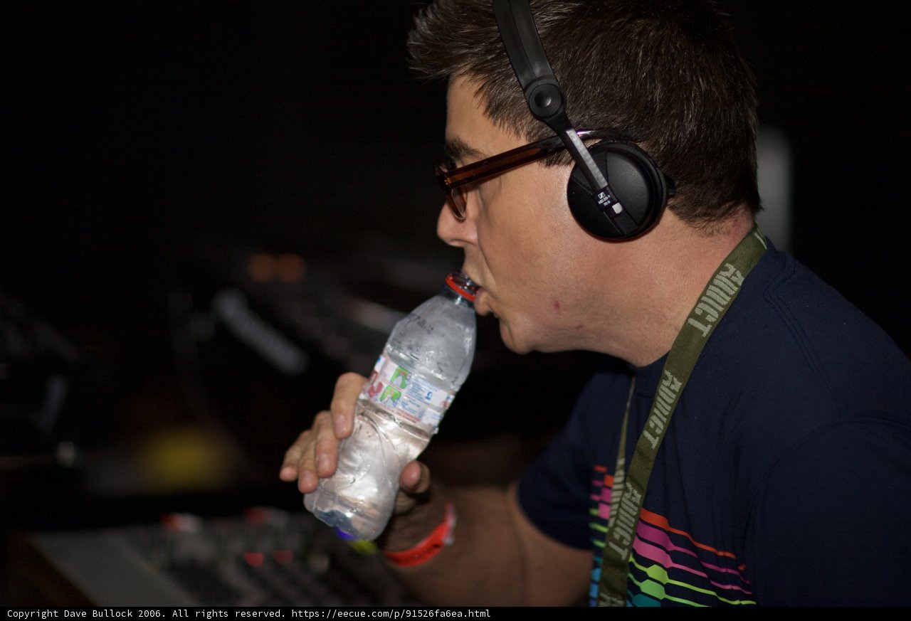 Refreshing Tunes Caption: A man takes a break to hydrate while listening to music with his headphones on.