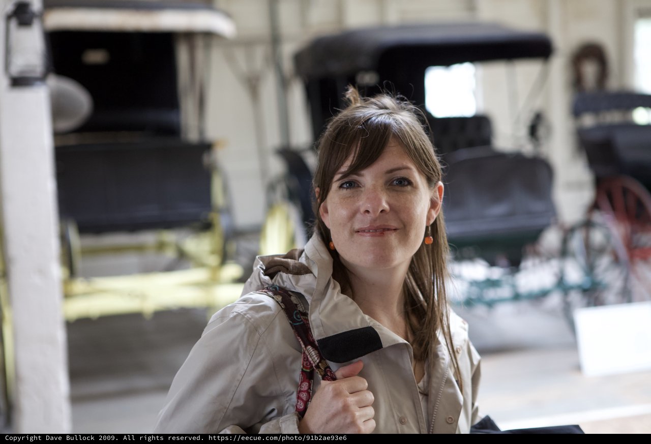 Woman Smiling Among Vintage Carriages in Museum