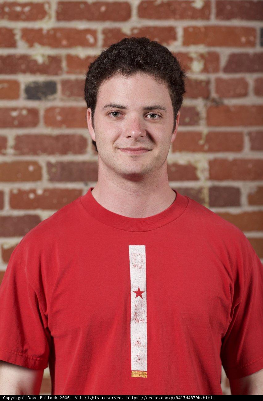 Red Shirted Teenage Boy Smiling in front of Brick Wall