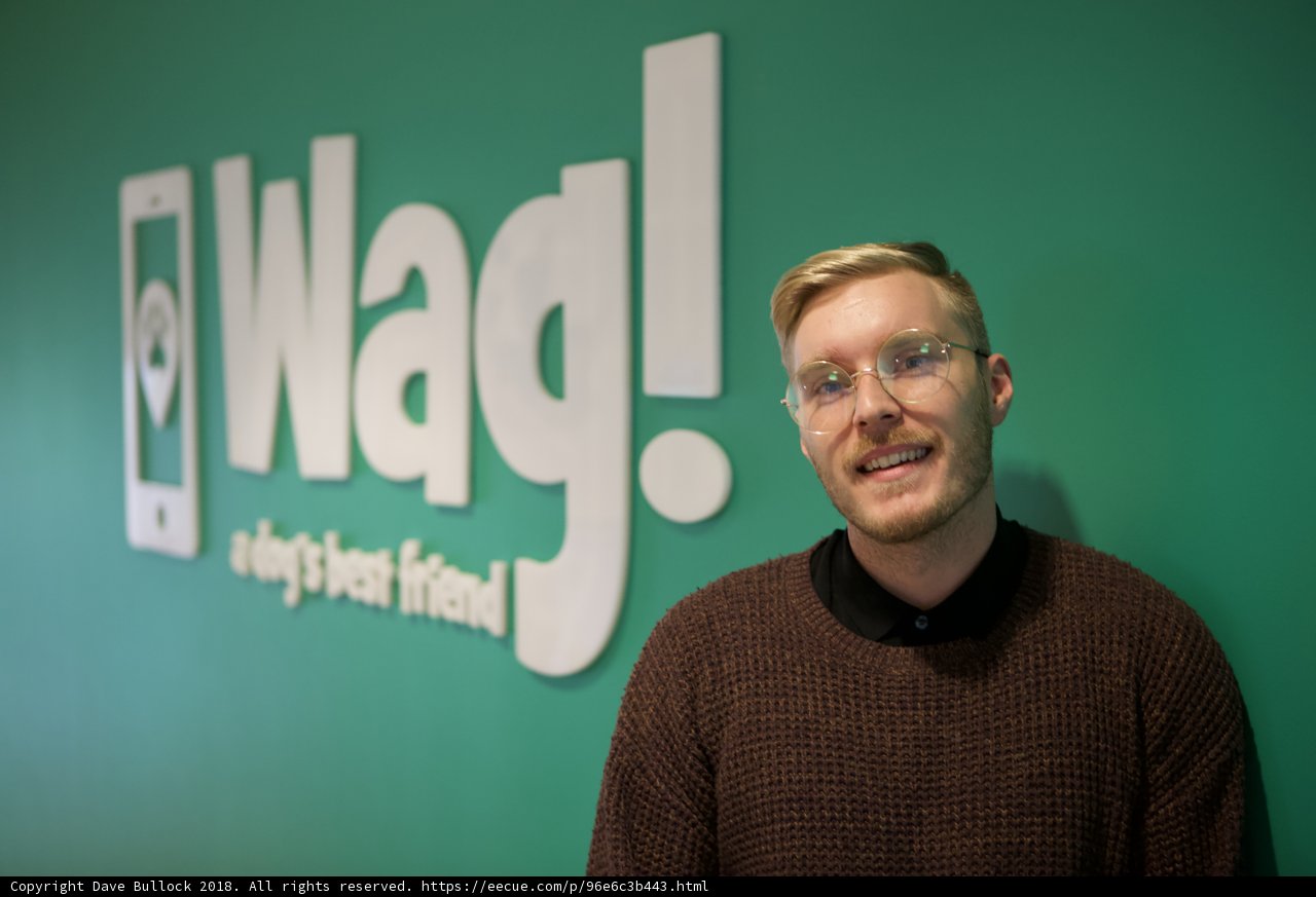 Stylish Man in Glasses Poses in Front of WAG Logo