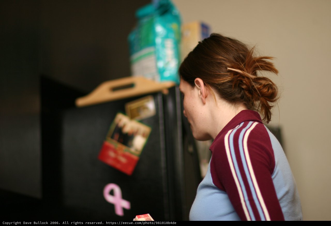 Young Woman Peering Into Black Refrigerator at Night