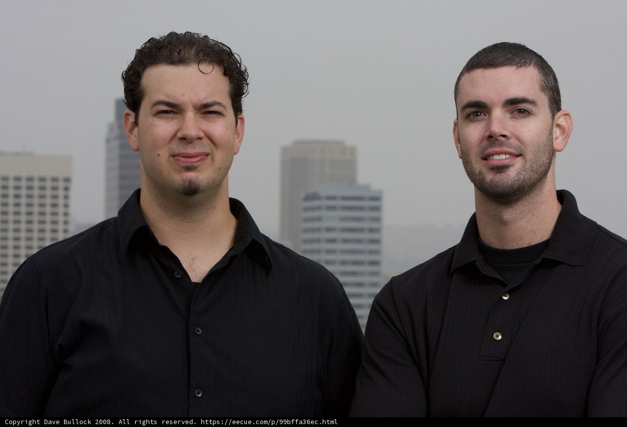 Two Happy Men in Black Shirts Pose in Front of Skyscraper