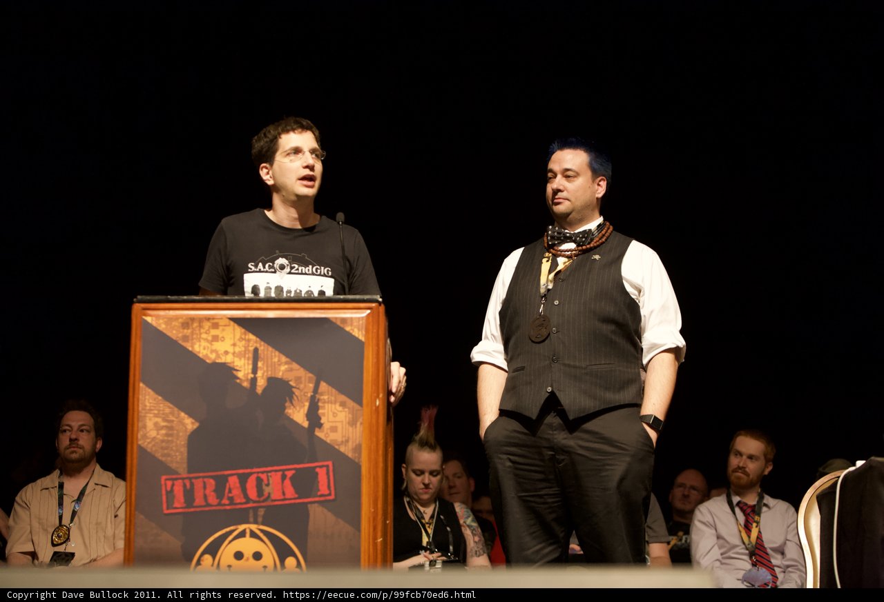 Two Men Deliver Speech At Podium While Crowd Listens