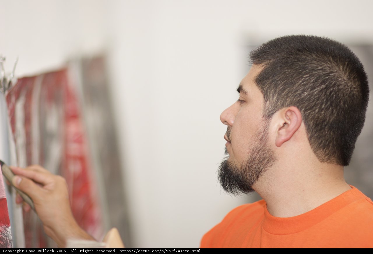 Wall Makeover Caption: A man gives a fresh coat of paint to his living room wall, using a brush held with his finger while his other hand holds the paint bucket.