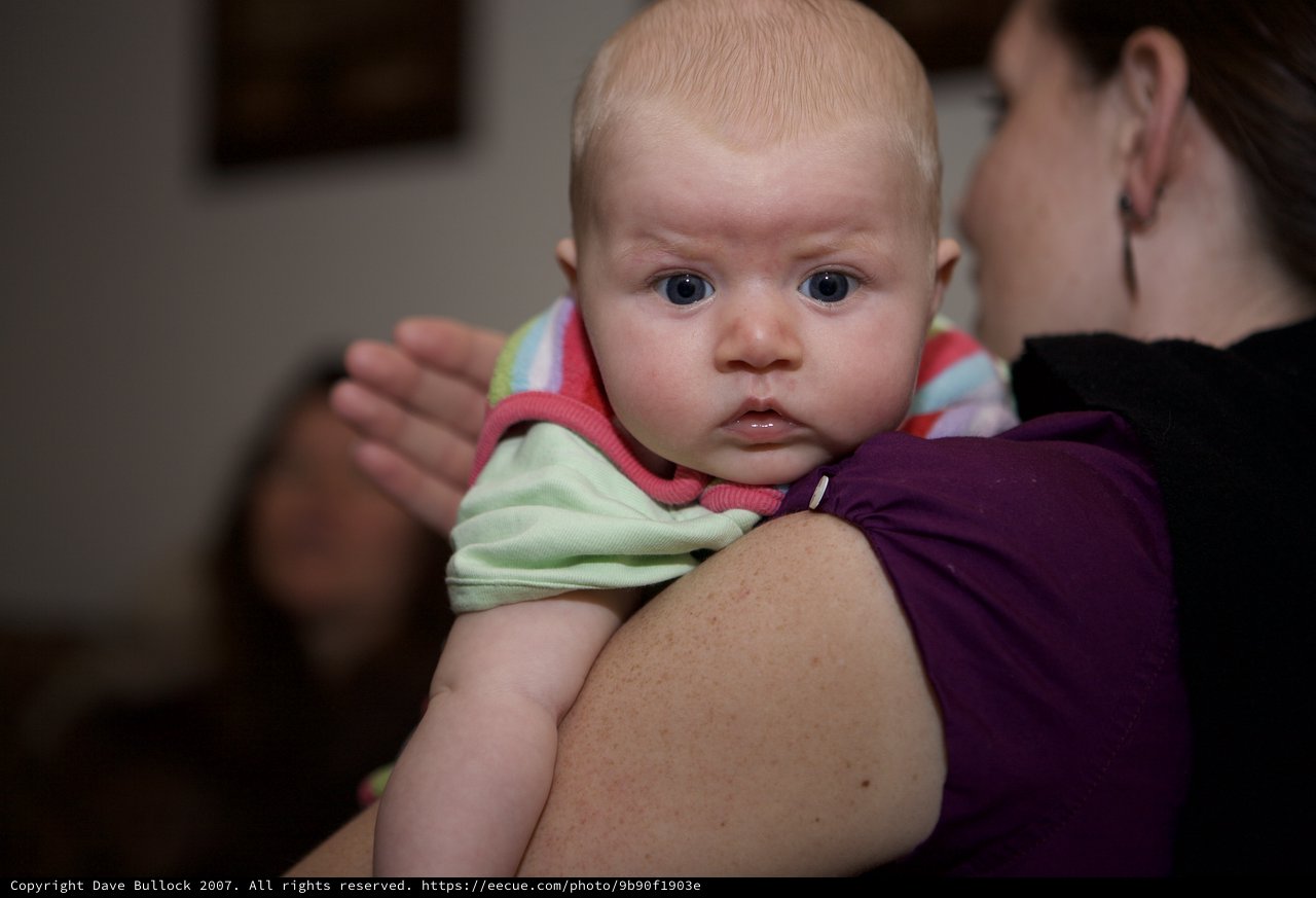 Wide-Eyed Baby Gazes Curiously Over Mother's Shoulder