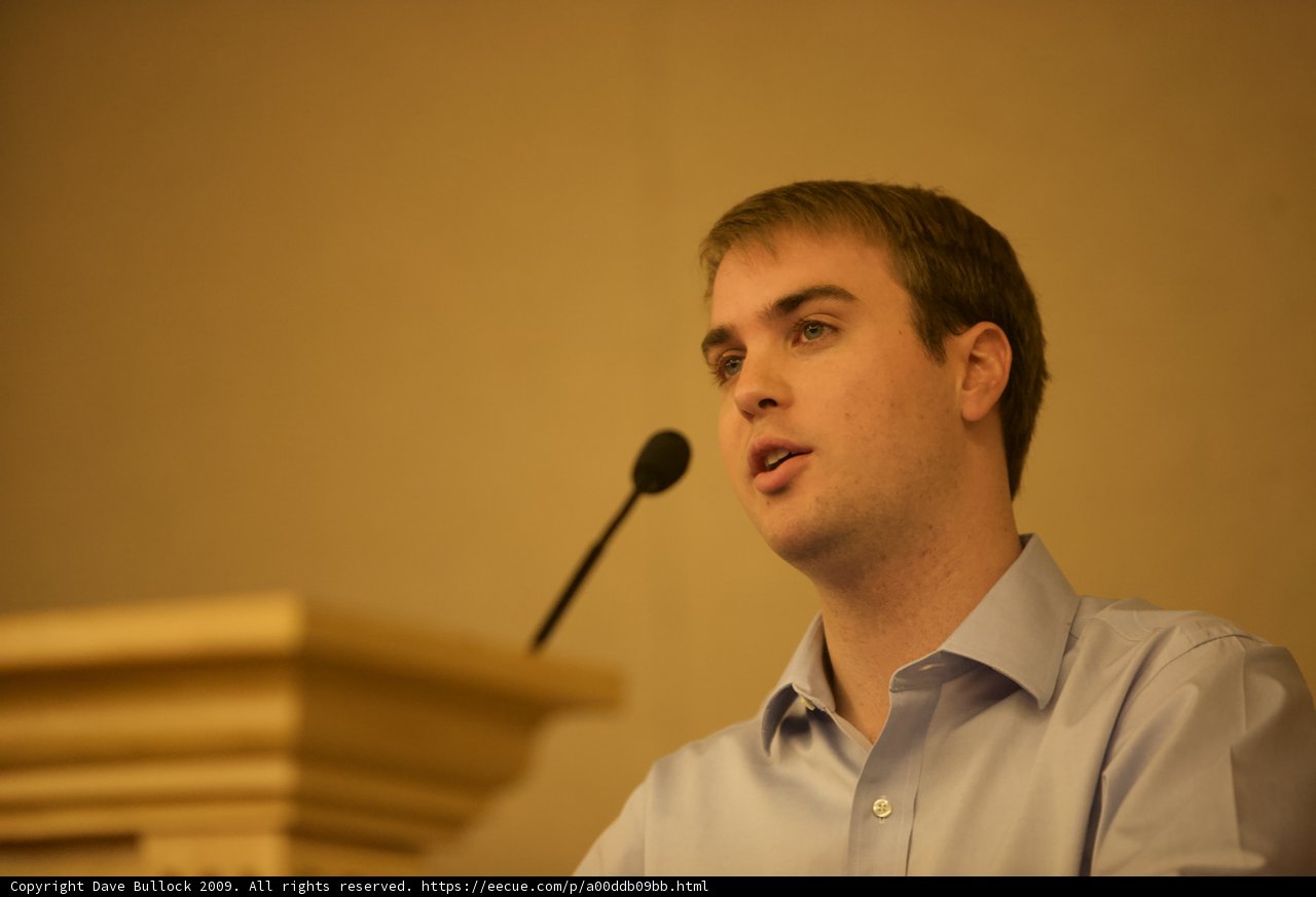 Blue Shirted Man Addresses Crowded Room