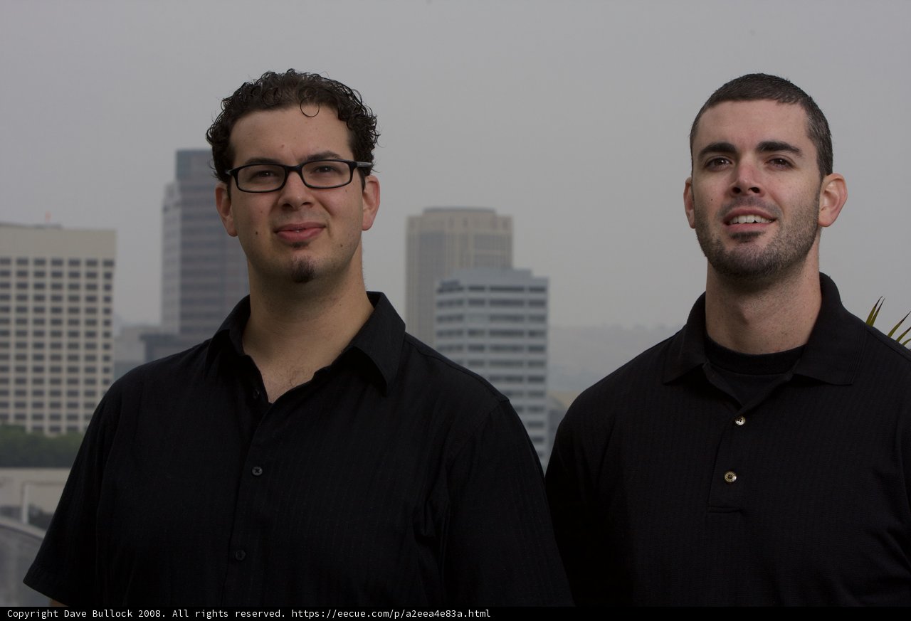 Two Happy Men in Black Shirts in Front of Skyscraper