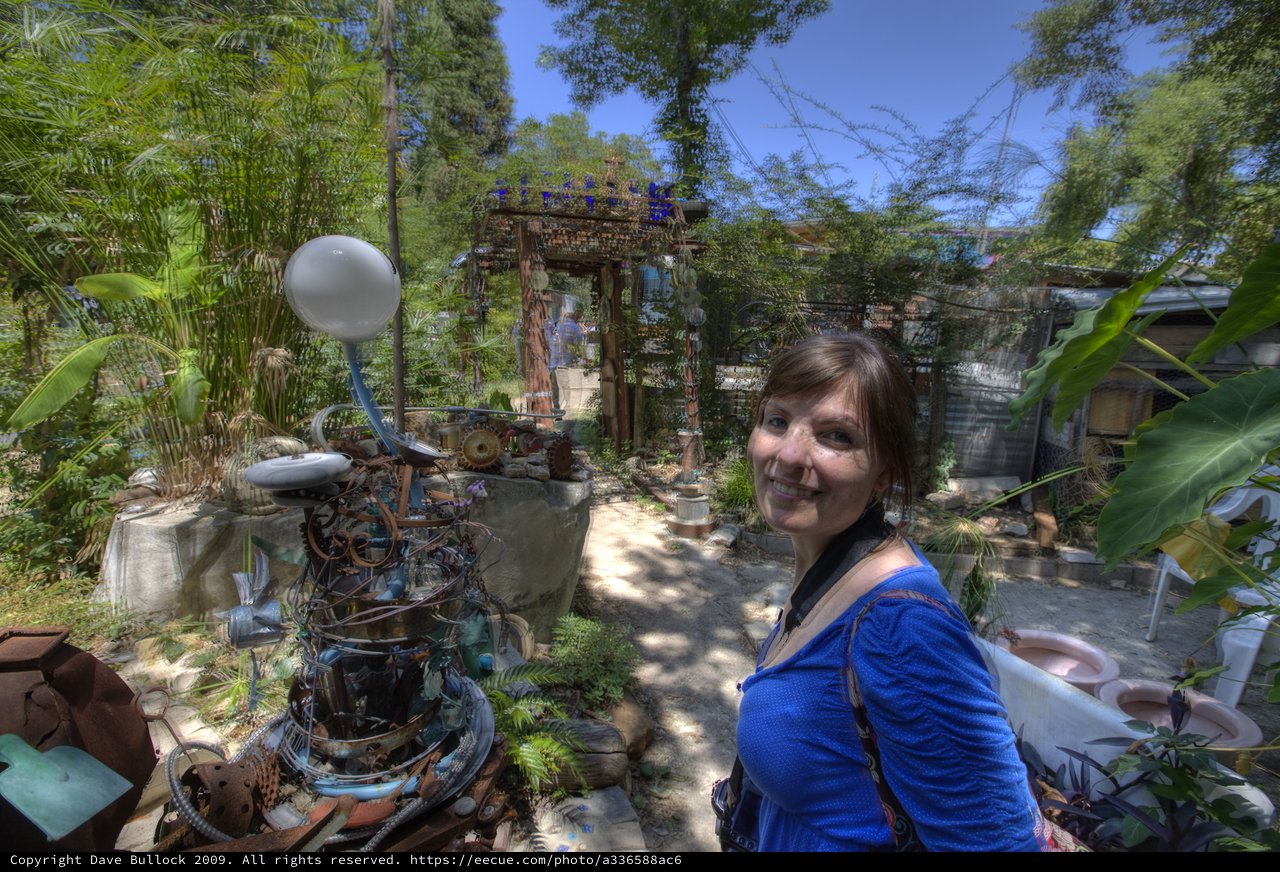 Woman Smiling Among Eclectic Junk Art Garden Sculptures