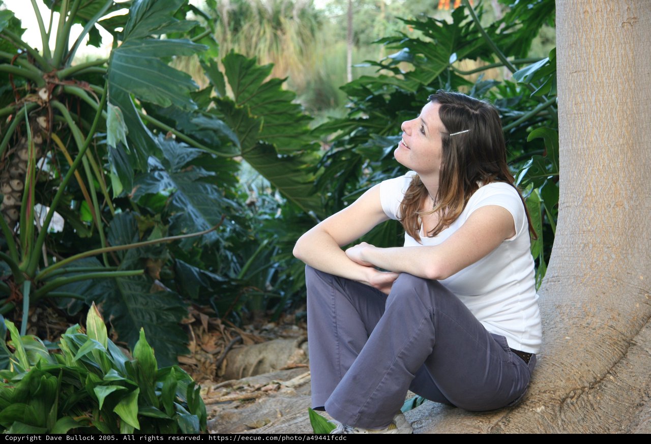 Young Woman Resting Against Palm Tree in Tropical Garden