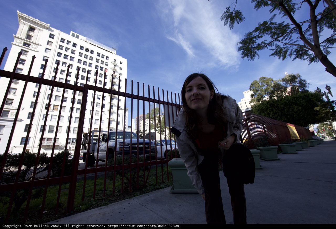 Woman Peering Through Iron Fence on City Sidewalk