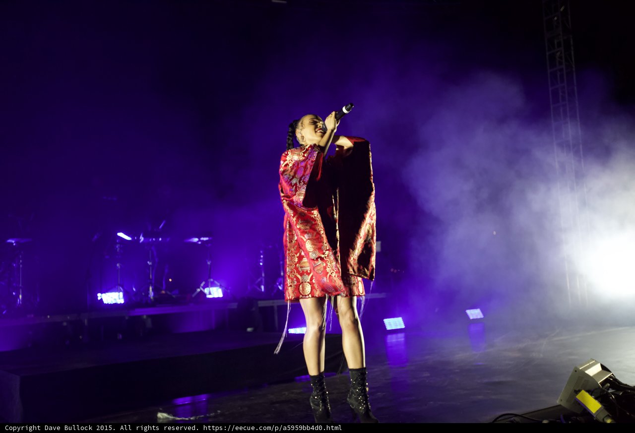 FKA twigs Full Body Standing Singing Microphone Raised High Looking Up Kimono Red Brocade Gold Patterns Beautifully Lit Black Boots Purple Lighting White Haze Band Drums Truss LED Panels