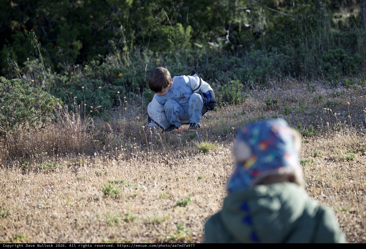 Young Explorer Crouching in Dry Grassland Field