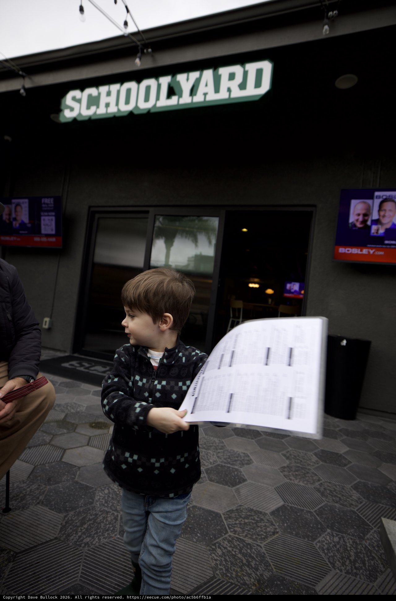 Young Boy Reading Sheet Music Outside Schoolyard Bar