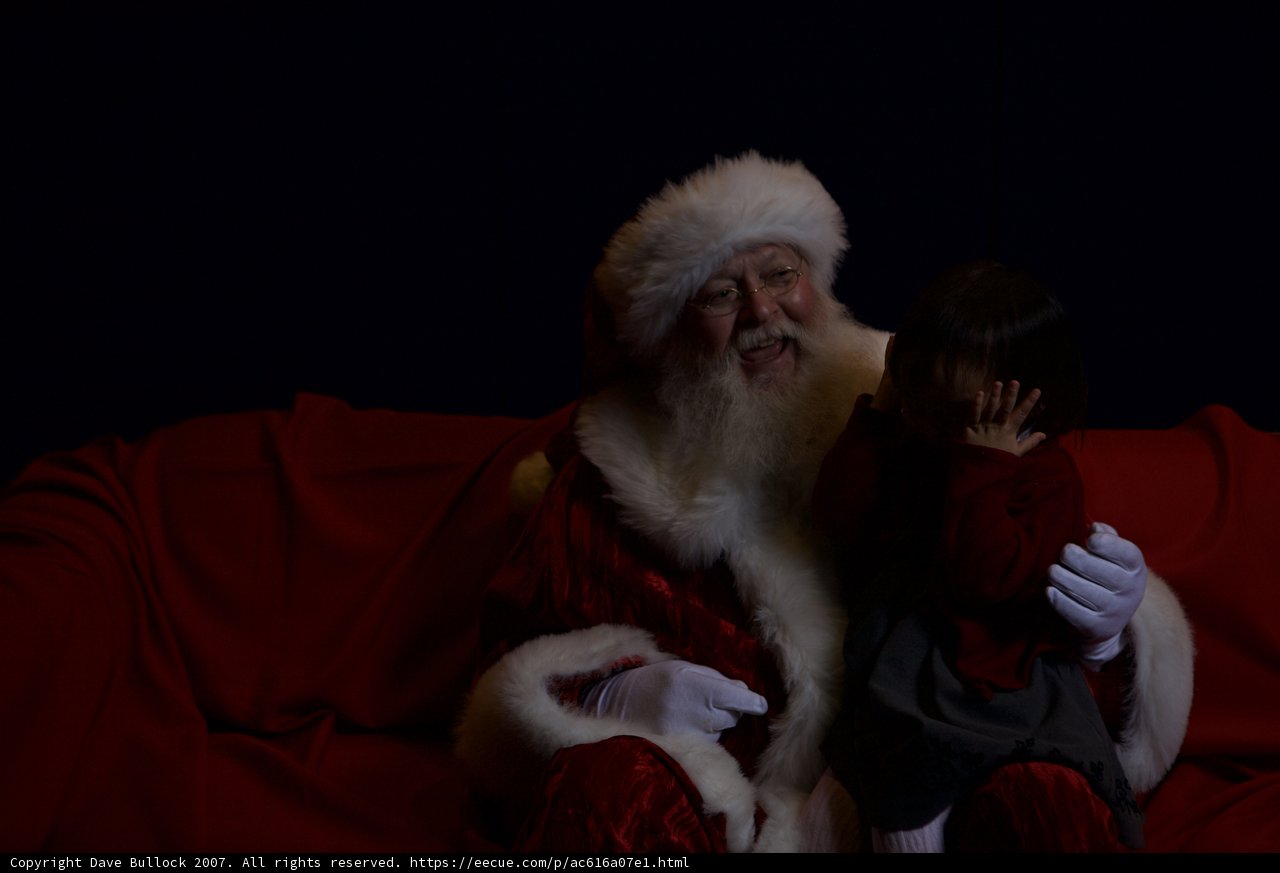 A Festive Santa Claus Taking a Break on a Red Couch with a Child