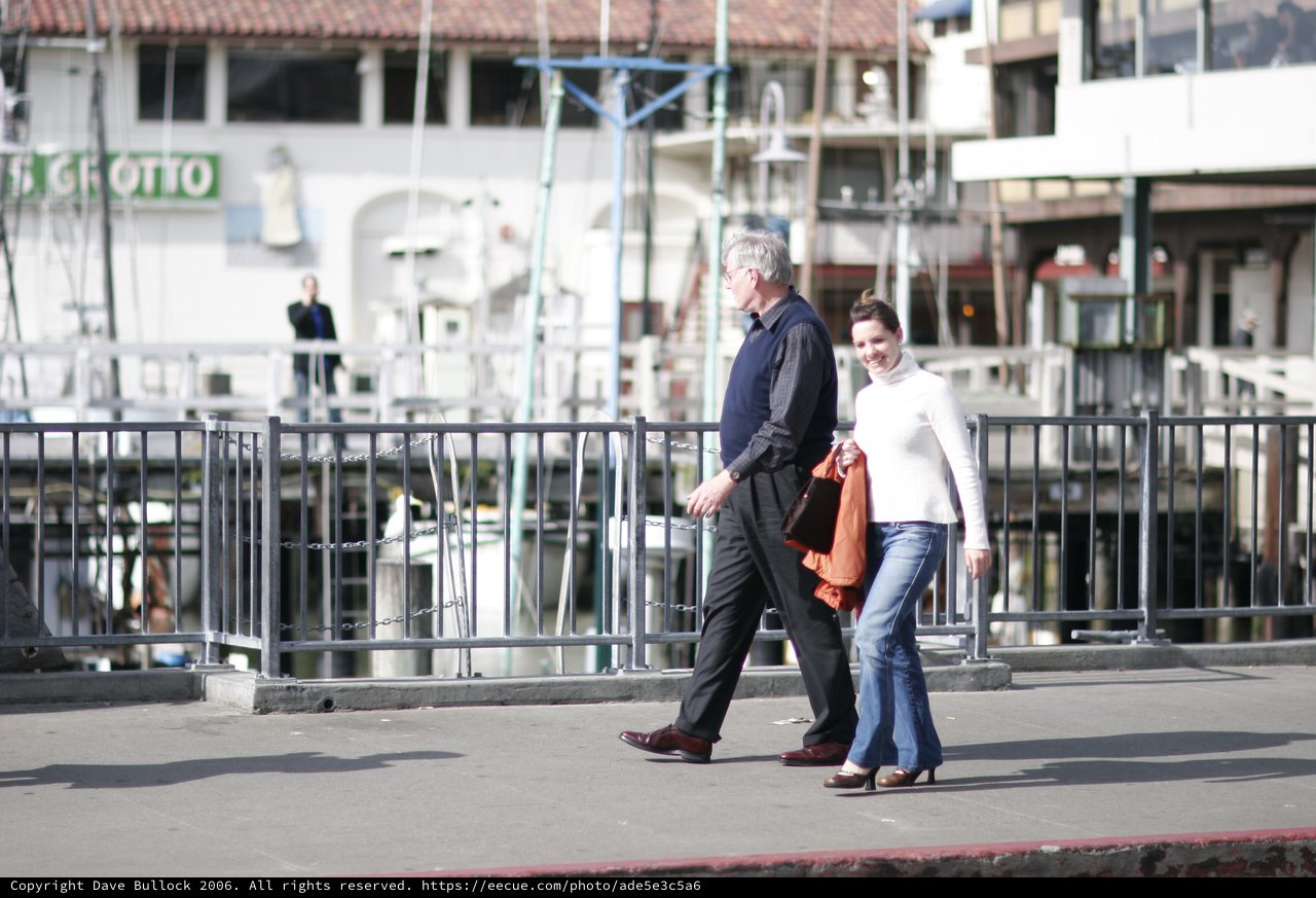 Couple Walking Along Waterfront Promenade in Bright Sunlight