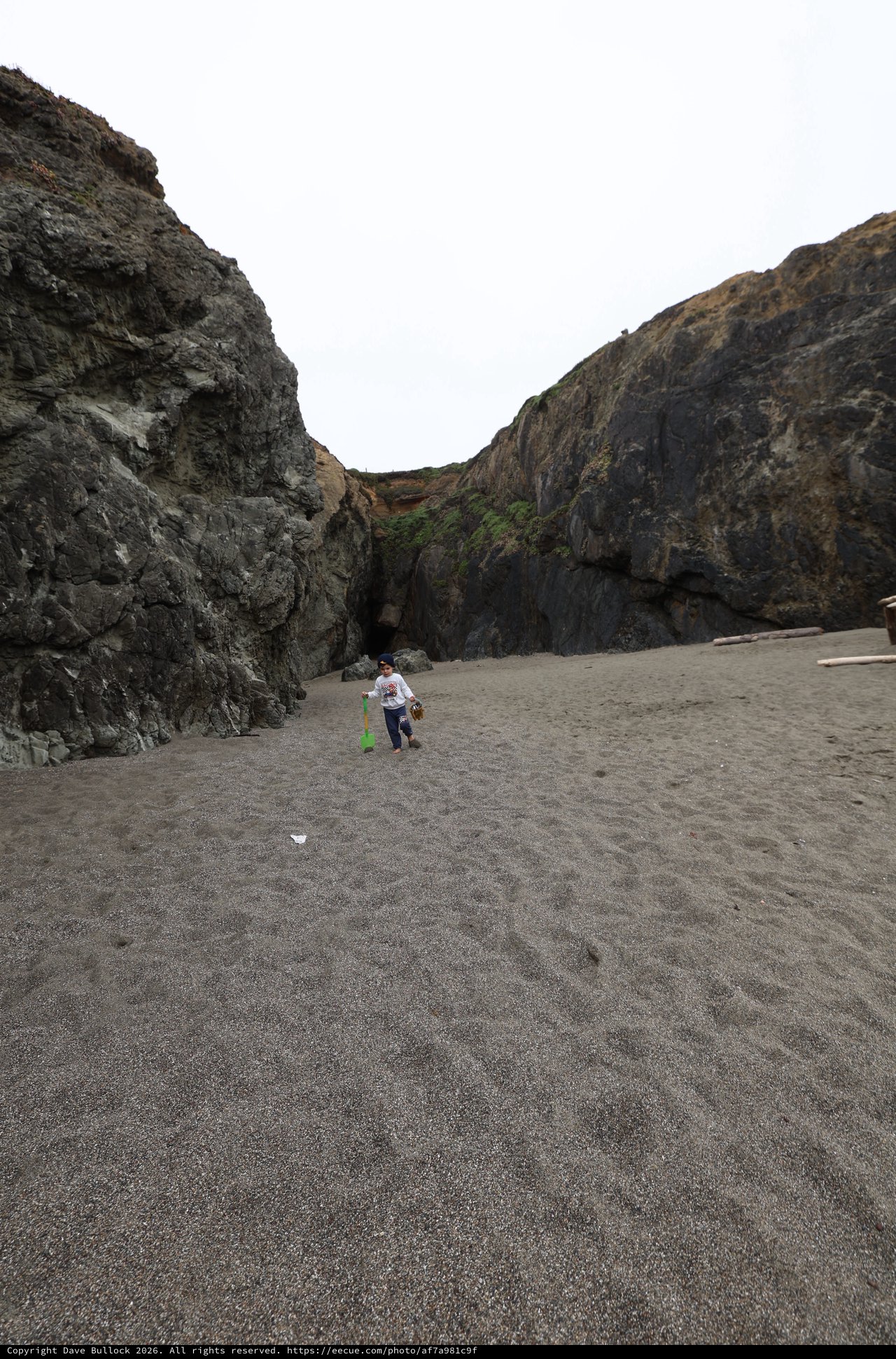 Child Explorer Between Sea Cliffs on Dark Sand Beach