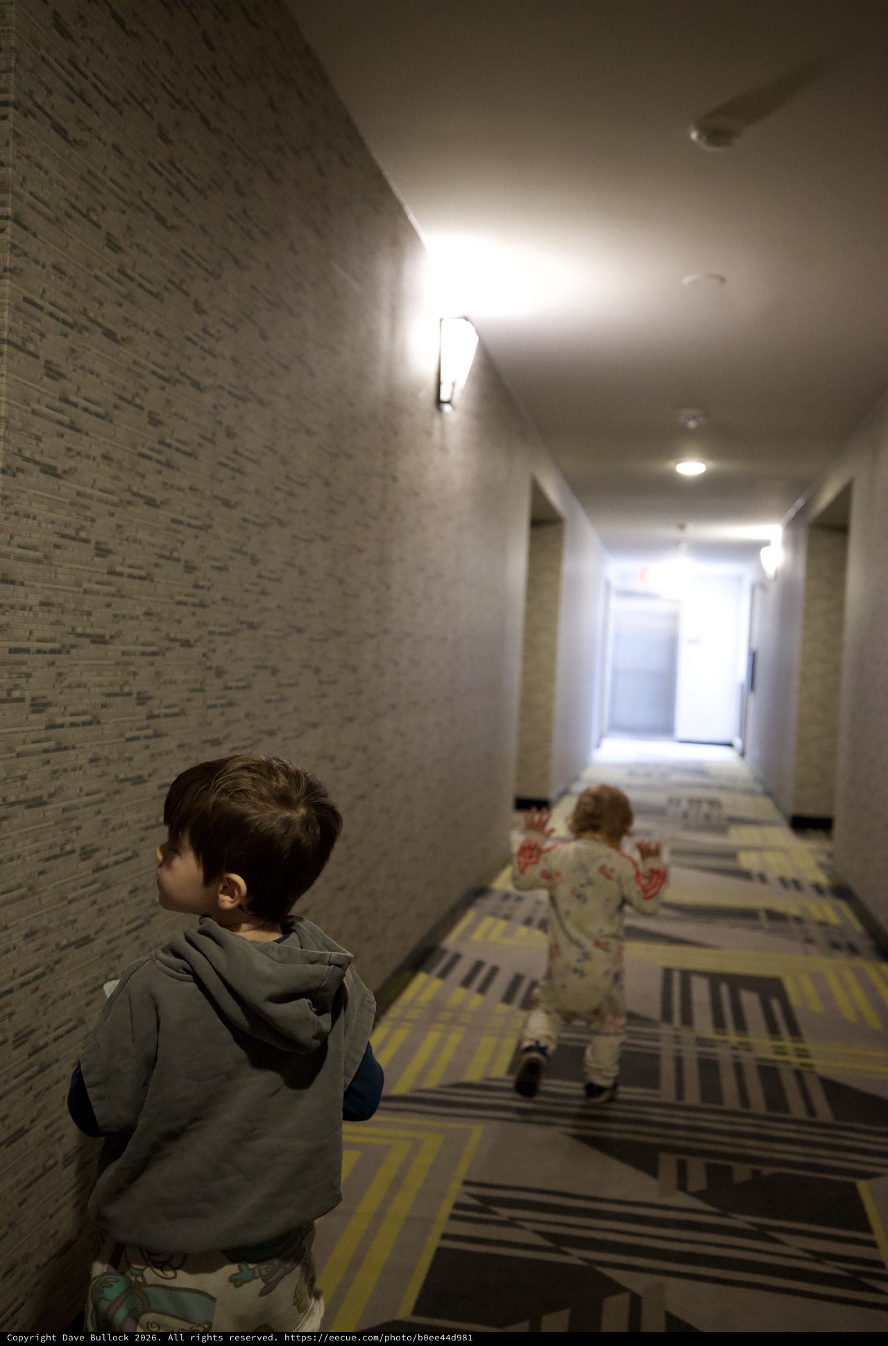 Two Children Running Down Modern Hotel Hallway
