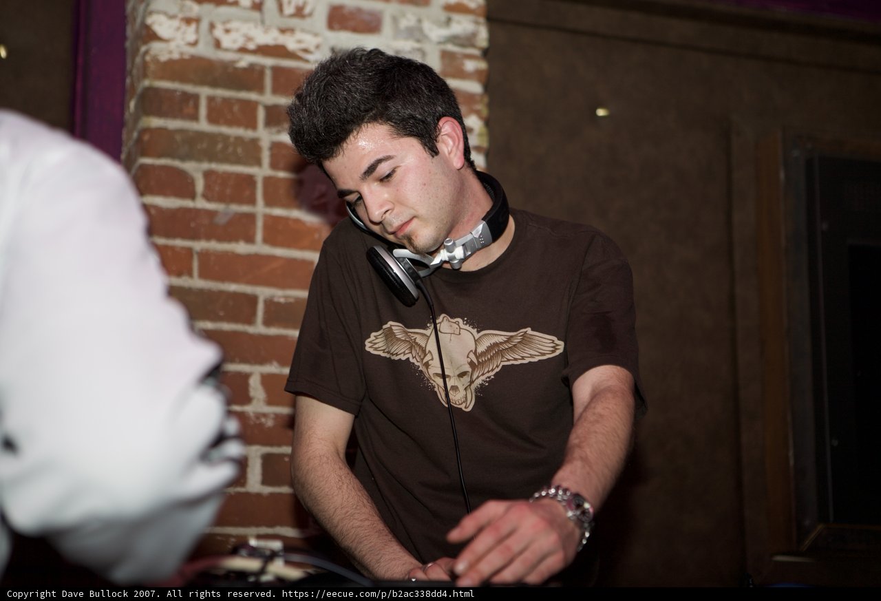 DJ Brownshirt brings the beats Caption: A man in a brown shirt shows off his DJ skills at Respect SF in 2007, surrounded by electronic equipment and brick walls.
