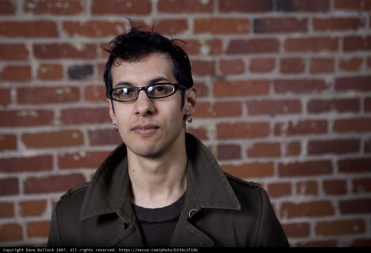 Smiling Man in A Jacket in Front of A Brick Wall