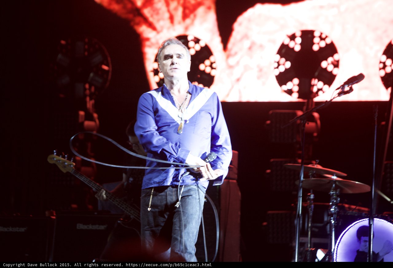 Morrissey Standing Holding Mic Cord Blue Shirt Bassist Drums LED Head Blackstar Circular Lights Red Screen