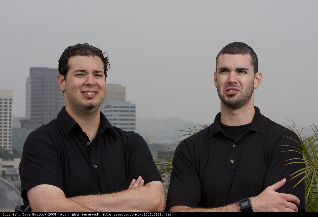 Two Smiling Men in Black Shirts Standing in a Cityscape