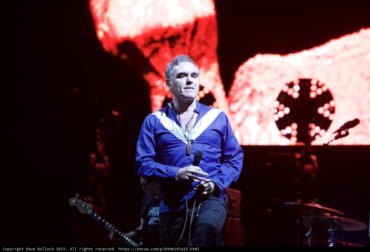 Morrissey Close Up Portrait Blue Shirt Necklaces Bassist Behind Circular Light Red Screen