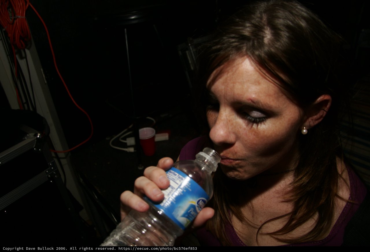 Woman Drinking Water Bottle in Dark Venue