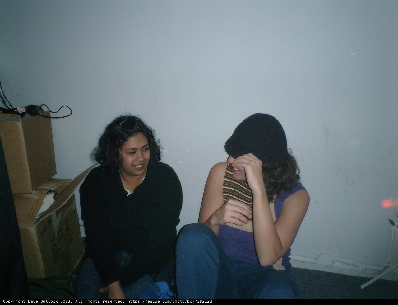 Two Women Lounging on a Bed Surrounded by Boxes and Clothing