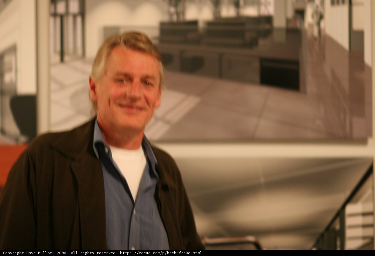 Man admires artwork in formal attire Caption: A man dressed in a coat, blazer, and tie stands by a handrail, smiling as he looks at a painting on a staircase in a beautifully designed interior of a house.