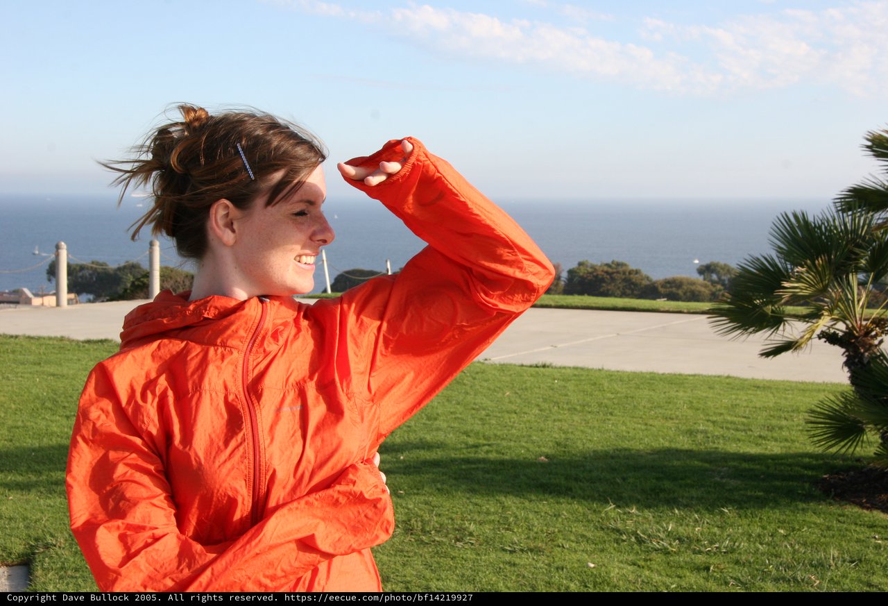 Windswept Woman in Orange Jacket by the Sea