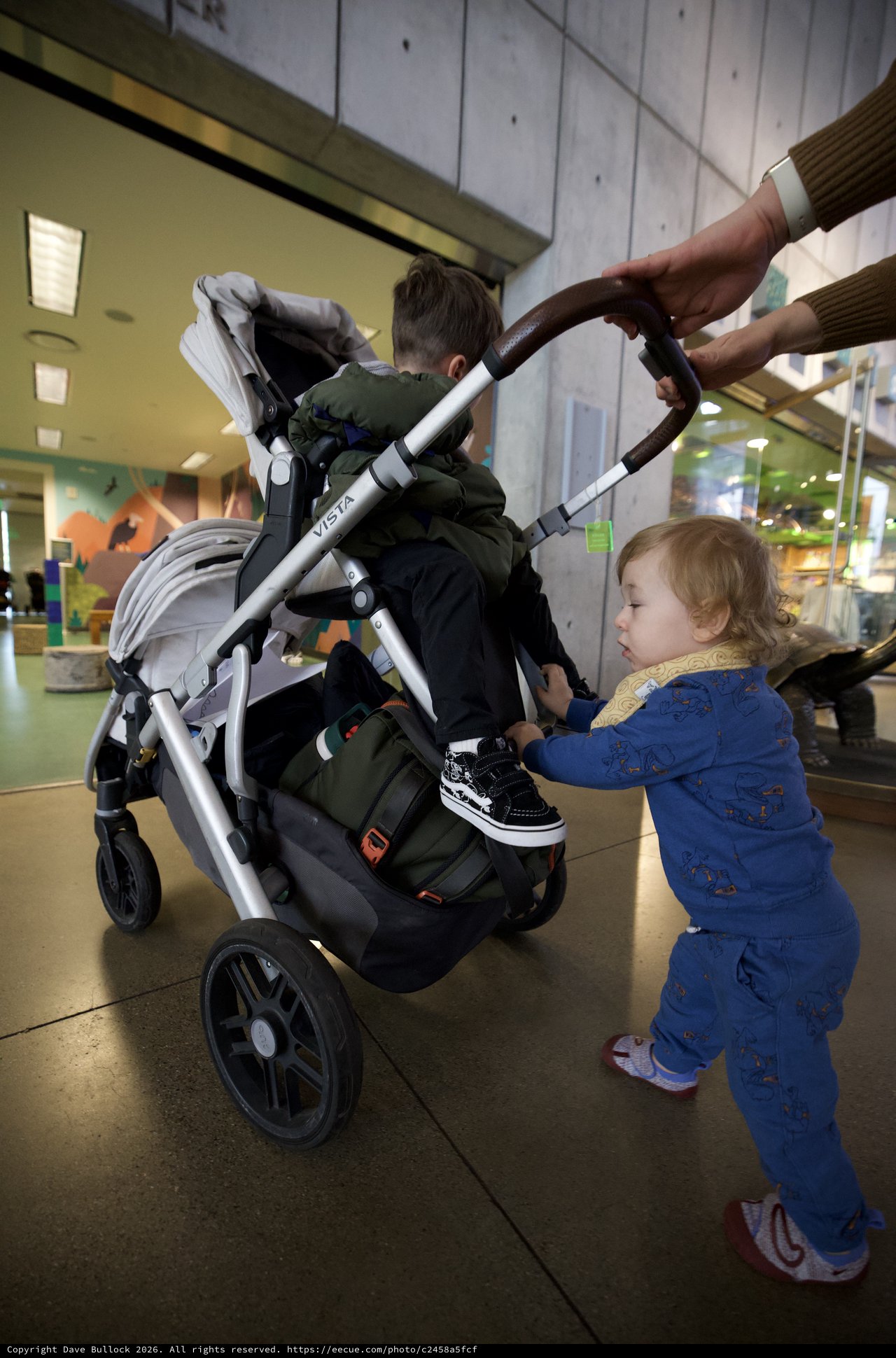 Toddler Helping Parent Push Stroller at Indoor Venue