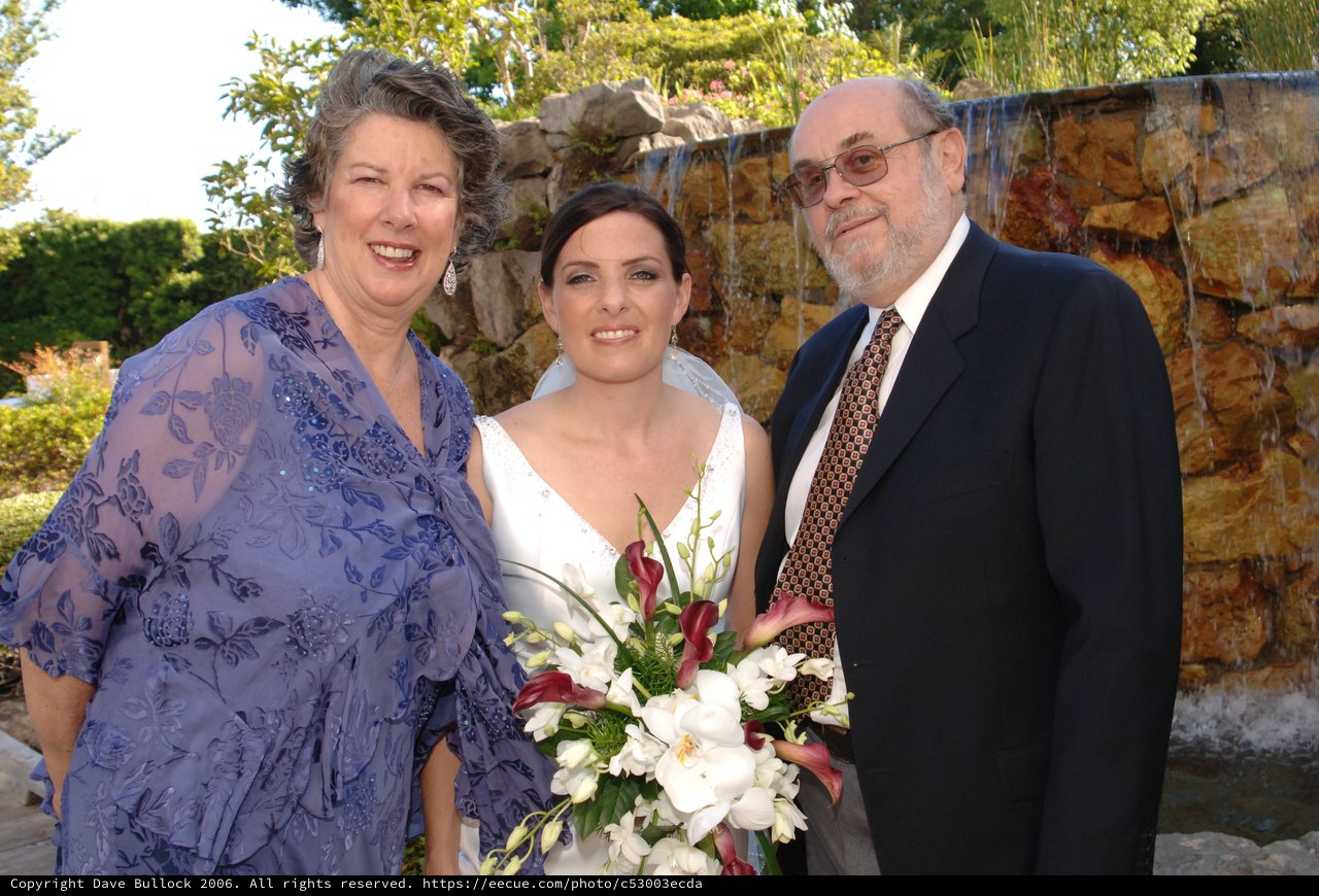 Bride Poses With Parents at Outdoor Wedding