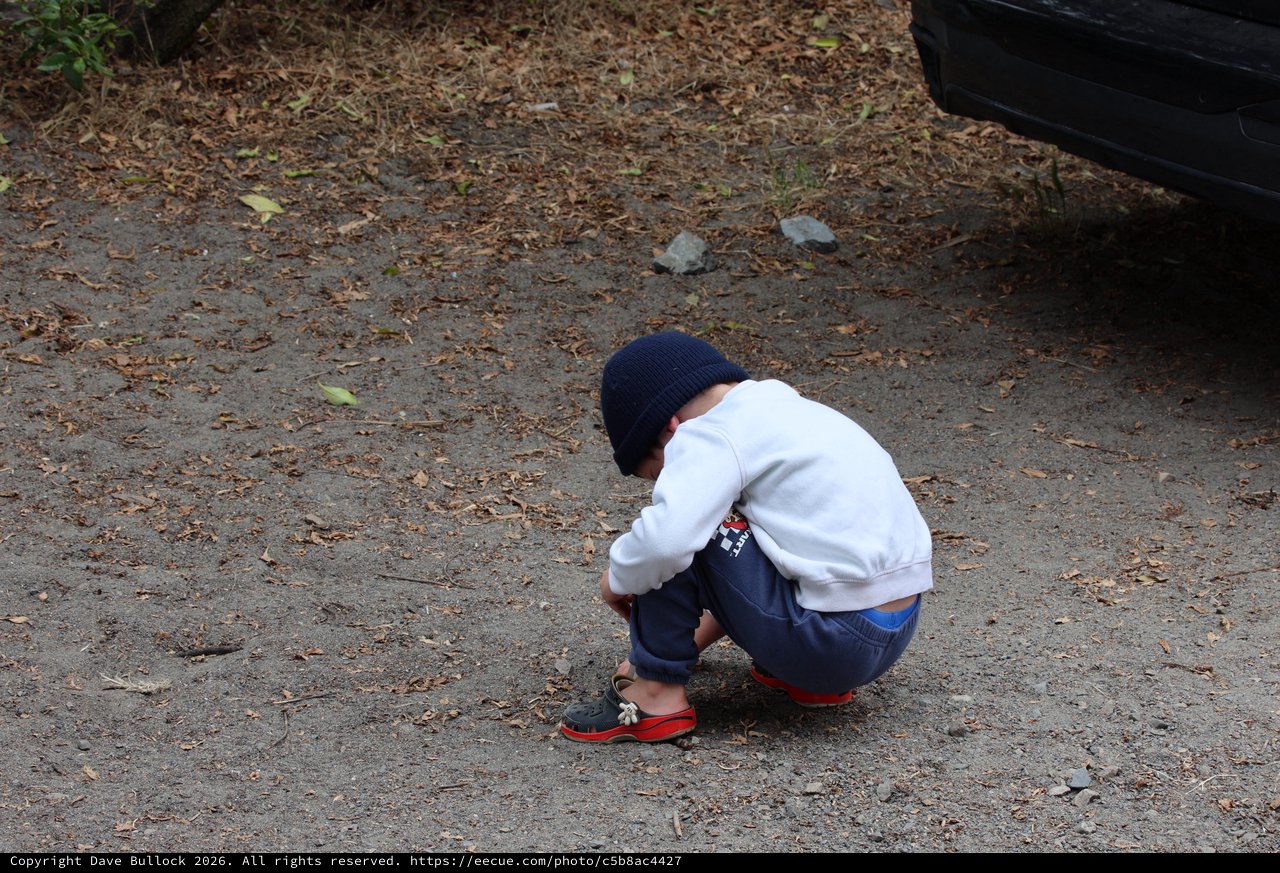 Young Boy Crouching in Curiosity on Dirt Path